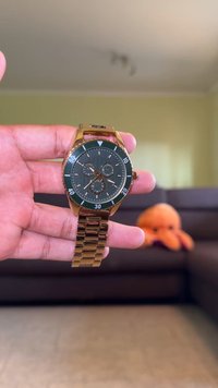 Gold-tone wristwatch with a round green bezel and dark green dial. Chronograph features, white hour markers, and metal link bracelet.