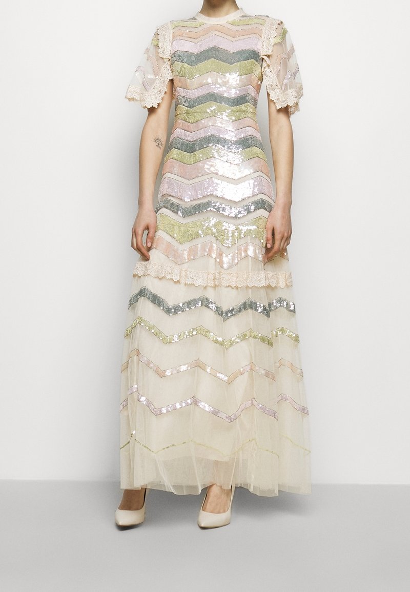 Femme portant une robe longue jusqu'au sol avec des manches en voile transparent et des sequins à chevrons horizontaux multicolores dans des tons pastel, ornée de dentelle.