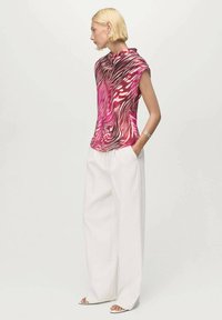 Top de manga corta en estampado animal en rosa y blanco, hecho de una tela ligera. Combinado con pantalones blancos sueltos. Cuello sencillo y corte relajado.