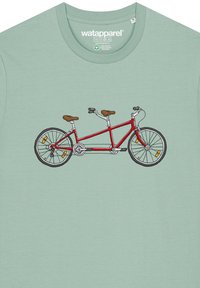 T-shirt vert clair avec un graphique de vélo tandem rouge, sièges marron, pneus noirs et réflecteurs orange. Design simple, dessiné en lignes.