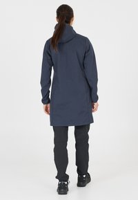 Mörkblå vattentät jacka med huva, långa ärmar och rak passform. Kombinerad med svarta byxor och stadiga skor. Slät textur, minimalistisk design.