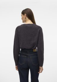 Pullover grigio scuro in maglia con maniche lunghe e scollo rotondo. Indossato sopra jeans blu a vita alta, evidenziando una vestibilità comoda e una texture morbida.
