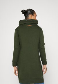 Lång sweatshirtklänning i olivgrön med hög krage, med läderdetalj på ryggen och ribbade muddar och fåll. Mjuk textur.