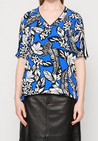 Top de manga corta con un fondo azul y patrones florales y de hojas en blanco y negro. Diseño de escote en V con un corte holgado.