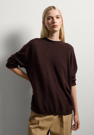 Maglione oversized marrone con scollo rotondo e maniche arrotolate, realizzato in un morbido tessuto testurizzato, abbinato a pantaloni beige.