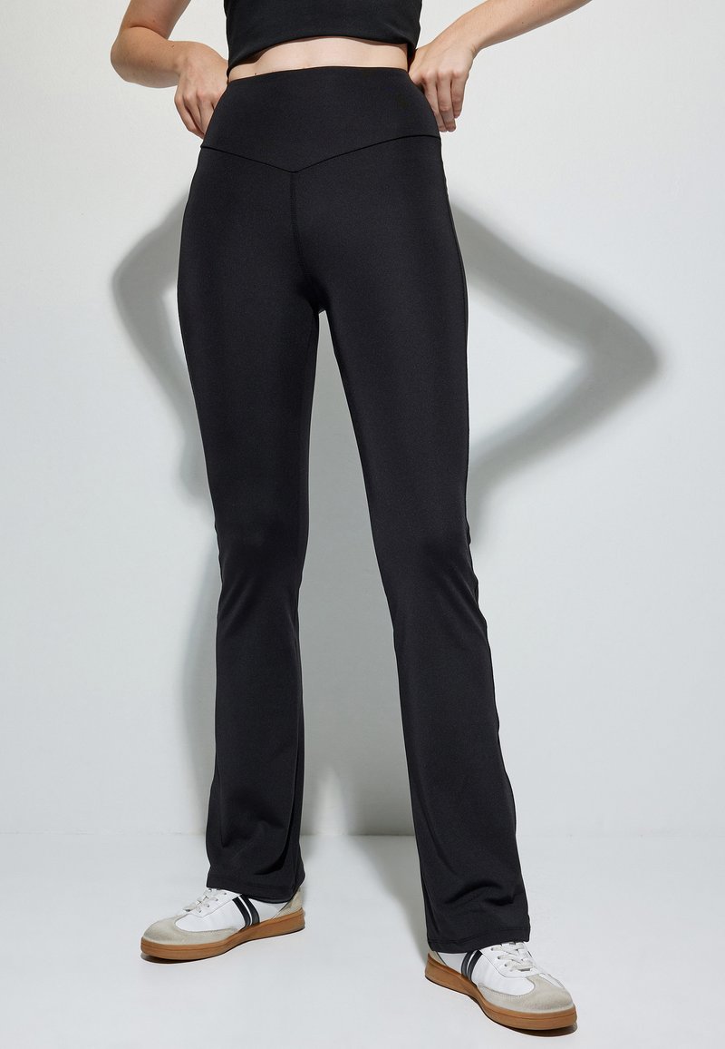 Zwarte, getailleerde leggings met een hoge, gecontourde tailleband; soepele, rekbare stof; licht uitlopende pijpen, gecombineerd met casual sportieve schoenen.