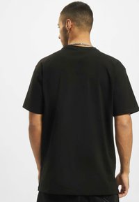 T-shirt noir à manches courtes avec un col rond, fabriqué dans un tissu lisse, présentant un design simple et une coupe décontractée. Pas de motifs visibles.