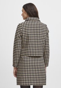 Beige ja mustriga houndstooth kasukas, millel on kraega kaelus, pikad varrukad ja kehasüstem. Puhas, hästikohandatud disain.