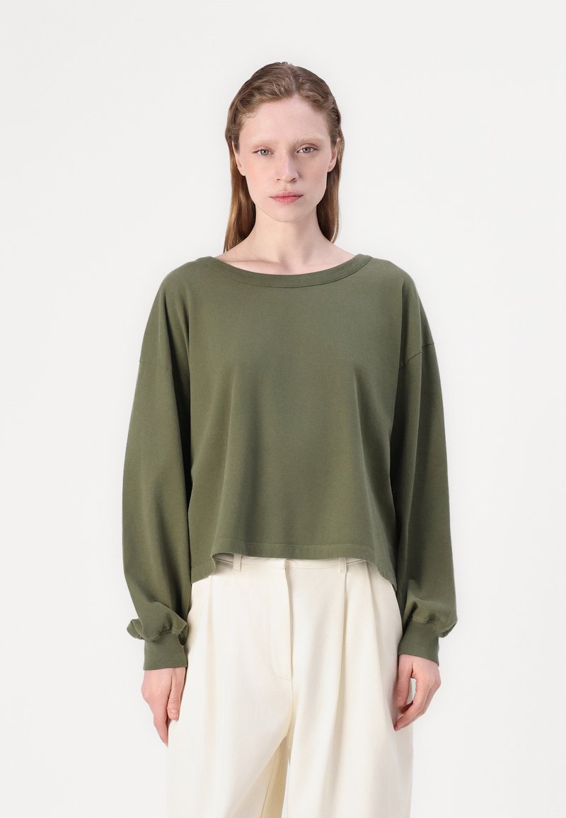 Oliva zöld hosszú ujjú crop top széles nyakkivágással és kényelmes szabással. Puha anyag, összegyűrt mandzsetták, fehér, laza szabású nadrággal párosítva.