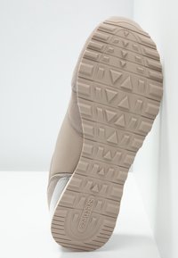 Beżowy sneaker z teksturowanym zamszowym i siateczkowym wierzchem, gumową podeszwą z geometrycznym wzorem trakcyjnym oraz logo na spodzie.