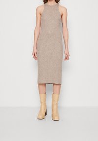 Strickad midiklänning i beige med ribbat mönster, med hög krage och figurnära design, kombinerad med krämfärgade blockklackade ankelboots.