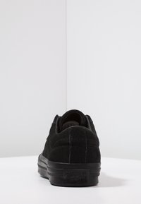 Zapatillas bajas de ante negro con un collar acolchado, costuras en contraste y suelas de goma, que presentan un logo en relieve en el talón.