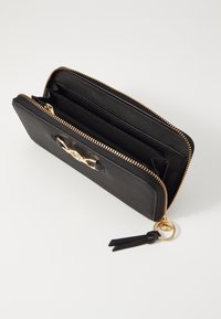 Cartera de cuero negra con cremallera dorada, múltiples compartimentos y un accesorio para llavero. Textura suave con un diseño minimalista.