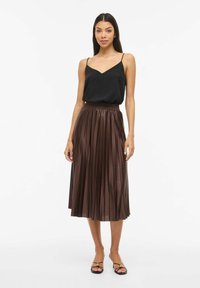 Črna brezrokavnik z tankimi naramnicami, kombiniran z visokim pasom, naborkasto, srednje dolgo rjavo krilo iz sijočega, teksturiranega materiala.