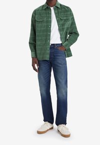 Grön rutiga knapp-up skjorta med två bröstfickor, i kombination med blå raka jeans och vita sneakers med en beige sula.