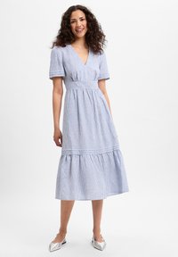 Gestreiftes Baumwollkleid mit V-Ausschnitt, kurzen Puffärmeln, tailliertem Bund und gestuftem Saum. Getragen mit silbernen Schuhen.