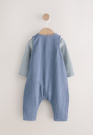 Blauwe gestructureerde overall met gestreepte lange mouwen, hangend aan een houten hanger tegen een lichte achtergrond. Focus op stof en kleurcontrast.