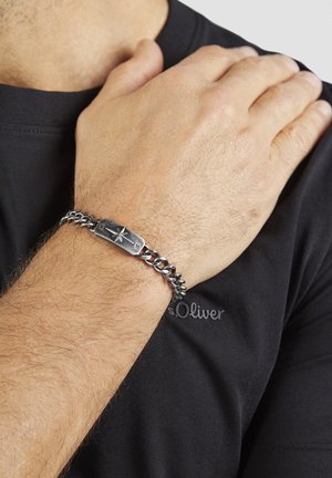 Silver-tone chain bracelet featuring an engraved central plate with a star design, worn on a wrist, against a black shirt.