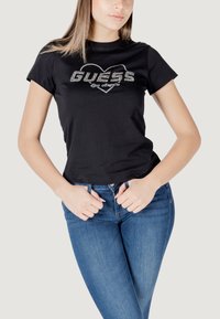 Zwarte katoenen t-shirt met korte mouwen en een cropped ontwerp, met een zilveren rhinestone "GUESS Los Angeles" logo op de voorkant.