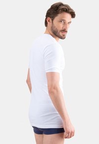 T-shirt blanc à manches courtes en tissu doux, design ajusté, encolure ronde. Le modèle le porte avec un short bleu marine.