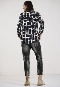 Navyblaues und cremefarbenes, gemustertes Hemd mit einem kastigen Design, kombiniert mit ausgewaschenen schwarzen Jeans und tanfarbenen Ankle-Boots. Sichtbare strukturierte Stoffe.