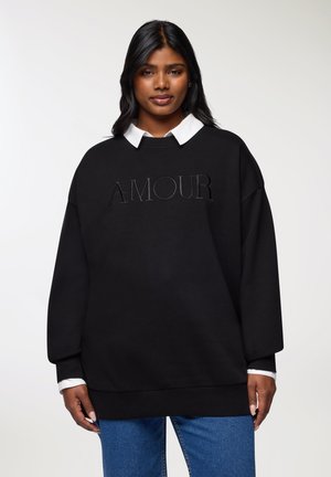 Felpa nera oversize con testo in rilievo "AMOUR" sulla parte anteriore, dotata di una camicia bianca con colletto sotto e polsini a costine.