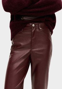 Burgundisk läderbyxor med en slät yta, som har en klassisk femfickdesign och silverknappdetaljer.