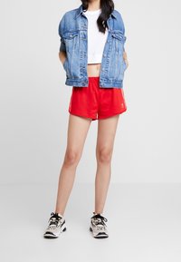 Giacca di jeans, t-shirt corta bianca, pantaloni sportivi rossi con strisce bianche e sneakers in bianco e nero con un motivo.