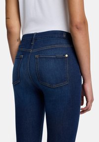 Mörkblå denimjeans med midjeficka, utrustade med bakfickor och kontrasterande gula sömmar. Slät textur och figurnära design.