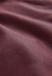 Bordo tkanina z gladko teksturo, z rahlim sijajem in finim, gostim tkanjem. Površina je videti rahlo zmečkana.