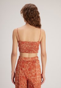 Top rojo recortado con textura fruncida y tirantes finos, combinado con pantalones anchos de pierna fluida en color naranja con un diseño floral.