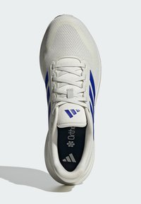 Zapatilla deportiva blanca con parte superior de malla, tres franjas azul marino y plantilla Ortholite. Presenta cierre de cordones y suela texturizada.