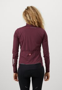 Bordová cyklistická bunda má vysoký golier, dlhé rukávy a zadné vrecká. Je vyrobená z hladkého, elastického materiálu s reflexnými detailmi.