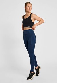 Svart sport-bh och marinblå högmidjade leggings gjorda av stretchigt tyg. Leggings har sidofickor och en slät, elegant textur.