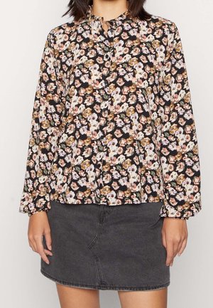 Schwarze Bluse mit floralen Motiven in Pink, Weiß und Braun, mit langen Ärmeln, Knopfverschluss vorne und einer lässigen Passform. Kombiniert mit einem dunkelgrauen Denim-Rock.