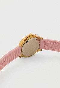 Sat zlatnog tona s ružičastim silikonskim remenom, sadrži poliran okrugli kućište, tri tipke za pritiskanje i teksturiranu površinu remena.