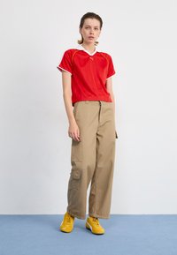 Red athletic shirt with white collar, khaki cargo pants with side pockets, and yellow sneakers with accents. Simple, casual outfit.