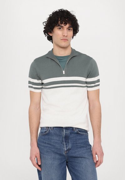 T-shirt med kort ärm och dragkedja i kragen, med en grön och vit färgblockdesign samt horisontella ränder över bröstet.
