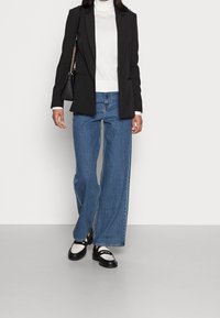 Veste noire, col roulé blanc, jeans larges bleu, et chaussures noires et blanches. Design simple, tissu lisse, et coupe décontractée.