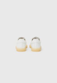 White leather sneakers with a low profile and rounded toe. Textured gum rubber sole, lace-up design, and minimalistic stitching details.