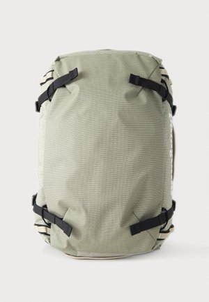 Sac à dos rectangulaire vert clair avec des sangles noires réglables à chaque coin sur un fond blanc uni.
