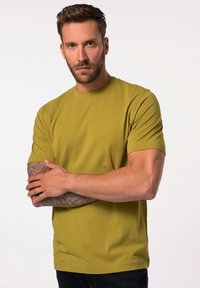 Olivově zelené tričko s krátkým rukávem v klasickém střihu, vyrobené z měkké bavlny s kulatým výstřihem a hladkým povrchem. Má tetované ruce.