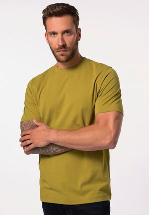 Camiseta de algodón de manga corta en verde oliva, con un corte clásico. Tiene un cuello redondo y una textura suave. Presenta brazos tatuados.