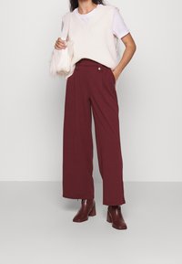 Överdimensionerad krämfärgad stickad väst över vit t-shirt, kombinerad med vinröda vida byxor och vinröda blockklackade ankelstövlar.