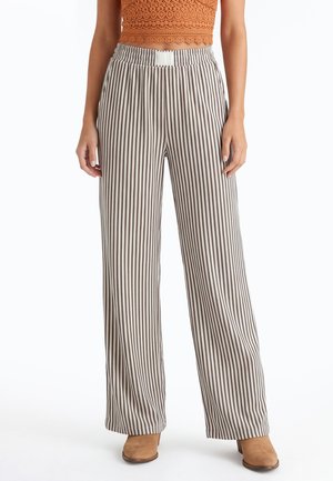 Bruin-wit met verticale strepen, wijde broekspijpen, gedragen met beige enkellaarsjes en een oranje mouwloos kanten cropped top.