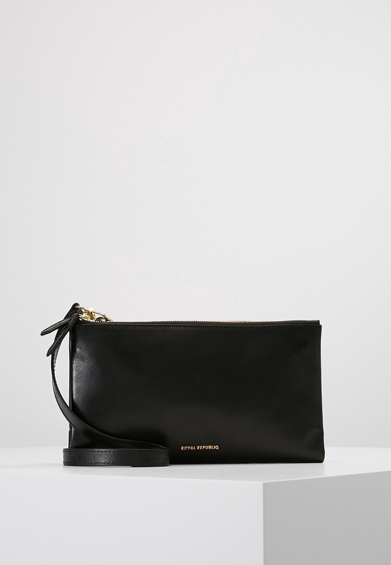 Bracelet rectangulaire en cuir noir avec fermeture éclair dorée et petit logo doré "Royal Republiq" sur le devant, posé sur une surface blanche.