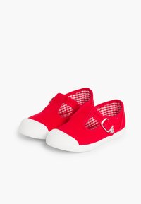 Zapatillas de lona rojas con suelas de goma blanca, que cuentan con una correa con hebilla y un diseño recortado. Interior forrado con un patrón de cuadros rojo y blanco.
