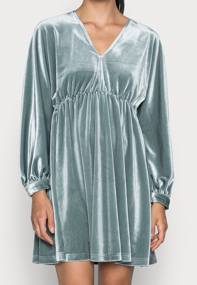 Sametové šaty v tlumené teal barvě s výstřihem do V, dlouhými nabíranými rukávy a elastickým pasem pro efekt shromážděné siluety.