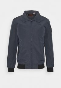 Veste bomber bleu marine avec une fermeture éclair frontale, des poignets côtelés et deux poches latérales. Comprend une poche zippée sur le bras gauche. Texture lisse.