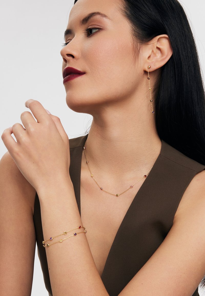 Zestaw biżuterii złotej składający się z naszyjnika, bransoletki i kolczyków z kolorowymi kamieniami, delikatnymi łańcuszkami i minimalistycznym wzornictwem.